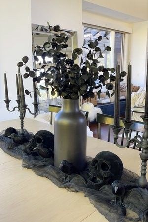 DIY monochromatic Halloween decor table setting featuring skulls, crows, candles, and eucalyptus